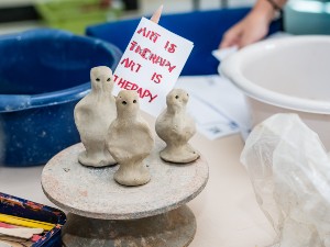 A photo of clay figures on top a clay spinning wheel holding a sign saying' Art is therapy' .