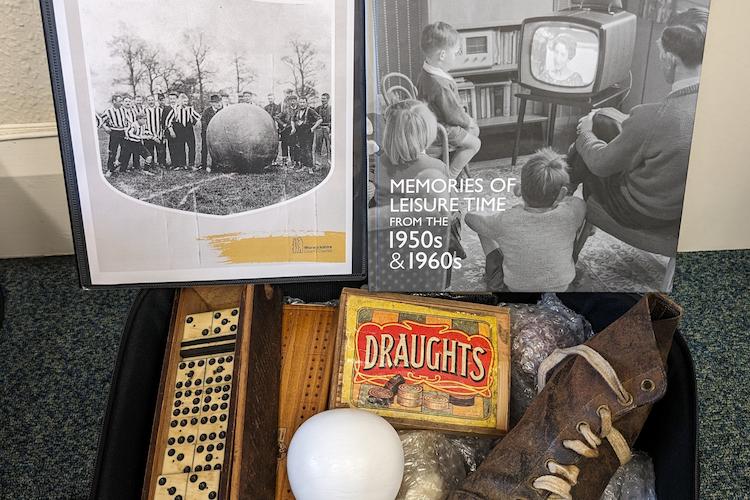 Image of a box containing leisure items from the 1950s and 1960s, including dominoes and football boots