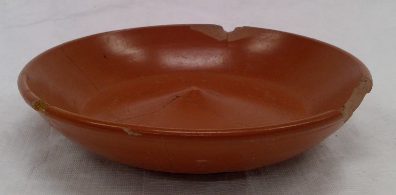 Old red bowl with thin cracks and a chip. The bowl as a upwards point in the middle of the base of it.