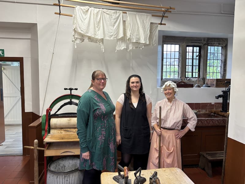 Three women smiling at the camera, stood in an old fashioned setting