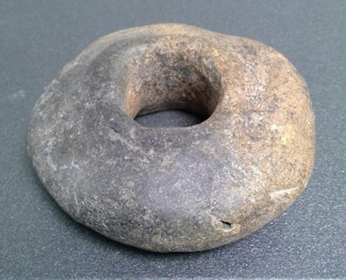 This donut-shaped object is made of baked clay and was used to weigh down the vertical threads (warp threads) on a loom.