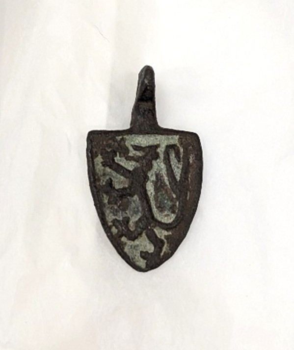 A small metal shield shaped badge or pendant which would have been attached to a horses harness.